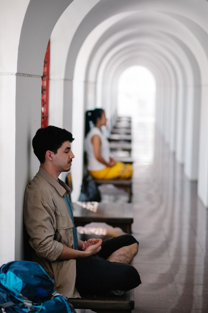 Man meditating with eyes closed in a serene arched hallway, embodying peace and mindfulness.